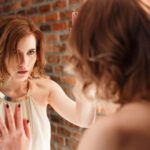 Beautiful red-haired woman intently desperate looks in the mirror.