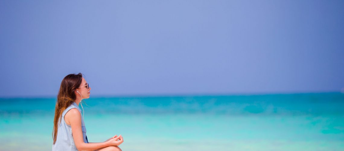 Beautiful woman in a meditation on the beach. Happy girl in yoga position relaxing on tropical beach