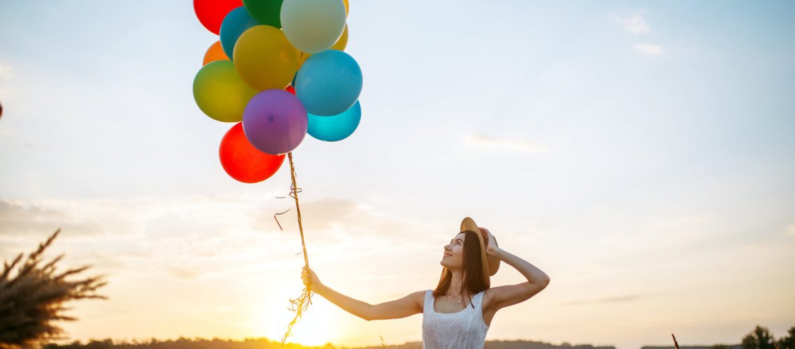 Woman releases balloons into the sky at sunset